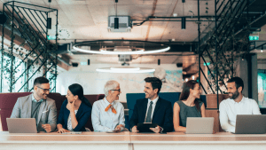 A row of both men and women professionals in front of their computers looking at each other and smiling